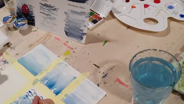 Hand malt mit Aquarellfarben auf Tisch.
