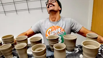 Mann lächelt hinter handgemachten Tontöpfen im Studio.