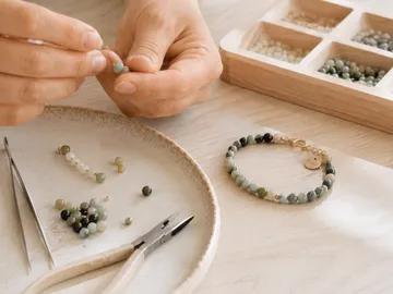Hände fädeln Perlen für Schmuck auf Teller.
