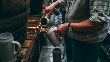 Person gießt Bier in einen Krug drinnen.