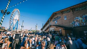 Menschenmenge genießt Fest neben Riesenrad draußen.