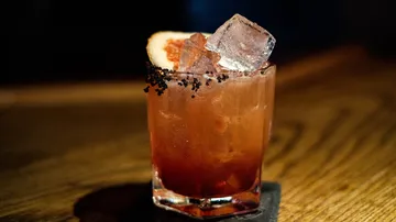 Cocktail mit Eis auf dunklem Holztisch.