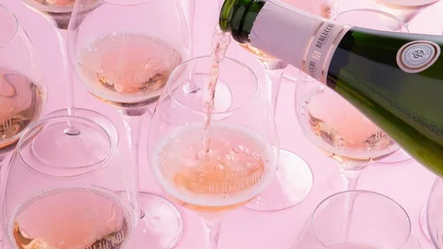 Champagne poured into glasses, pink background.
