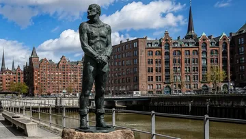 Statue eines Mannes neben Kanal, historische Gebäude.