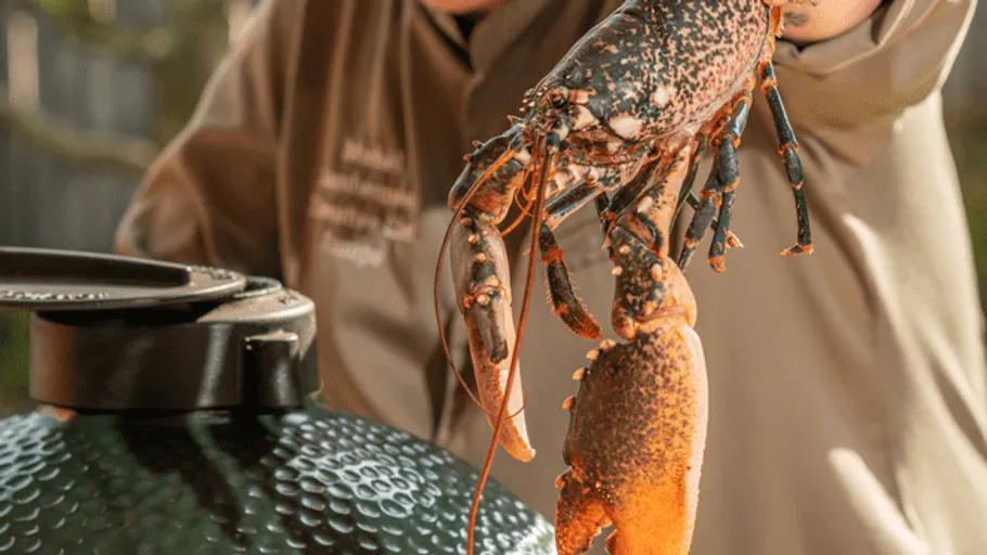 Lobster in a man's hand in front of a grill.