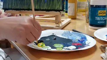 Hand mischt Farbe auf Palette nahe Staffelei.