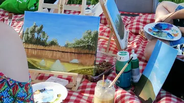 Paintings on easels during outdoor picnic.