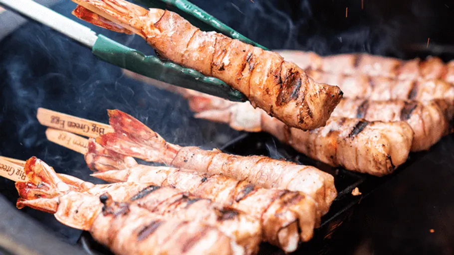 Grilled prawns are turned with tongs.