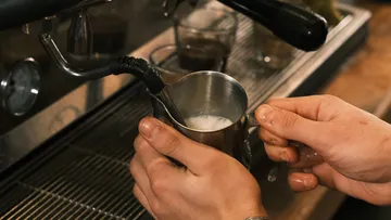 Hände schäumen Milch mit Espressomaschine auf.