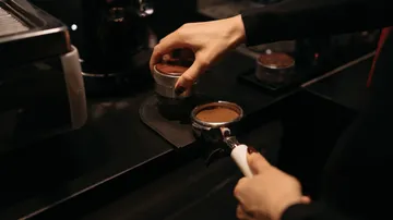 Hands preparing espresso with coffee tamper.
