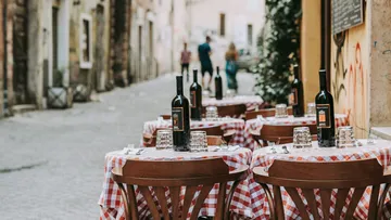 Open-Air-Café-Tische mit rot karierten Tüchern, Weinflaschen.