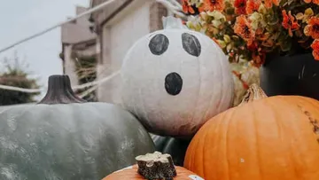 Pumpkins decorated; ghost face; surrounded by flowers.