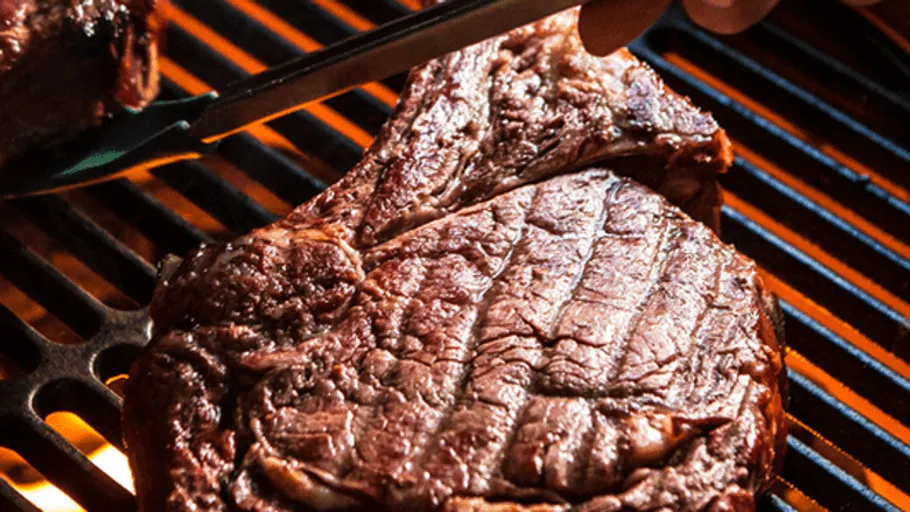 Steak wird auf dem Grill mit Zange gedreht.