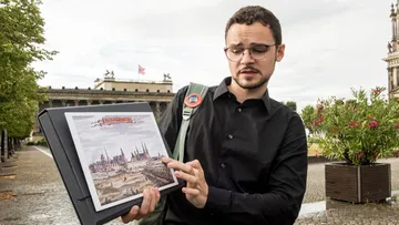 Person hält und zeigt historische Zeichnung draußen.
