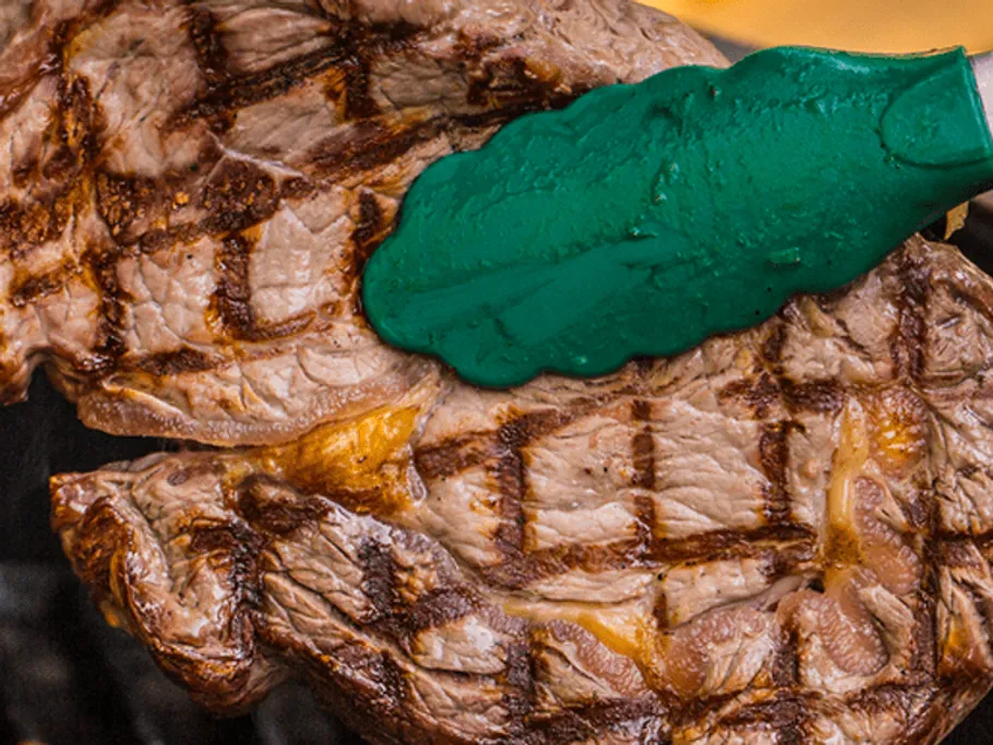 Grilled steak is turned with a green spatula.
