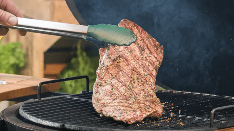 Fleischstück wird mit Zange auf dem Grill gewendet.