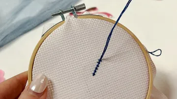 Embroidering on white fabric with blue thread.