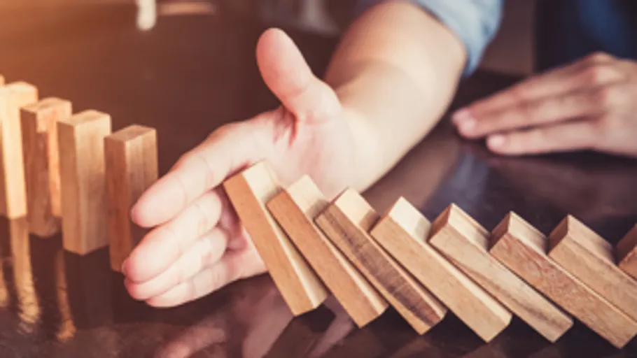 Hand stoppt fallende Dominosteine auf Tisch.