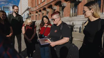 Person zeigt Buch Gruppe vor Gebäude.