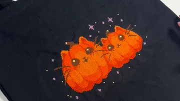 Orange cats embroidered on black fabric.