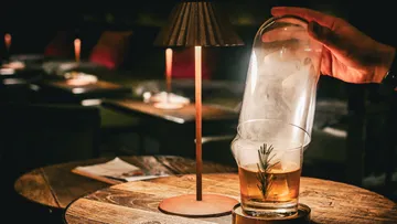 Hand lifting glass dome, cocktail underneath.