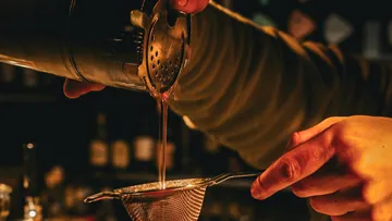 Bartender pours drink through strainer at bar.
