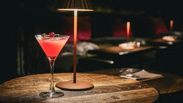 Cocktail glass on table in dim bar.