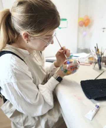 Person painting a decorative glass object indoors.