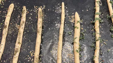 Breadsticks lined on baking sheet with herbs.