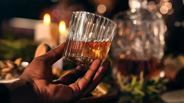 Hand hält Whiskyglas, Kerzen leuchten.
