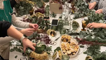 Personen basteln Kränze an dekoriertem Tisch.