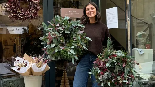 Woman holding wreaths outside a shop.