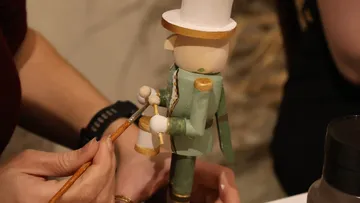Hand painting a wooden nutcracker indoors.