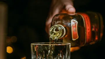 Hand gießt Whiskey in Glas, dunkler Hintergrund.