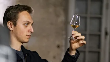 Person examining whiskey in a glass indoors.