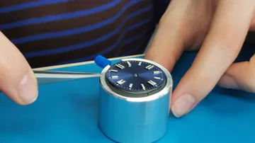 Watch dial assembly using tweezers in workshop.
