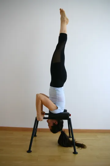 Frau macht Kopfstand auf Yoga-Stuhl.