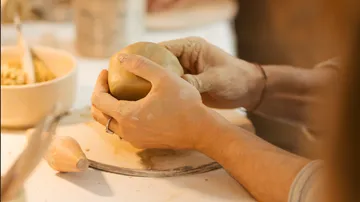 Hände formen Ton auf Töpferscheibe.