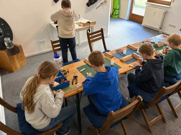 Children crafting wooden items indoors at table.