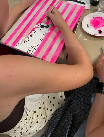 Person paints Dalmatian on pink striped canvas.