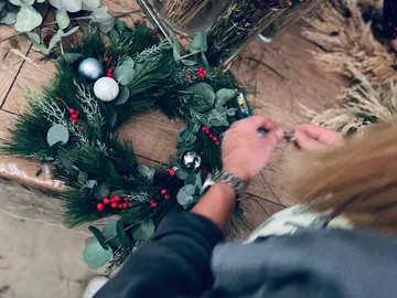 Person crafting festive wreath on table.