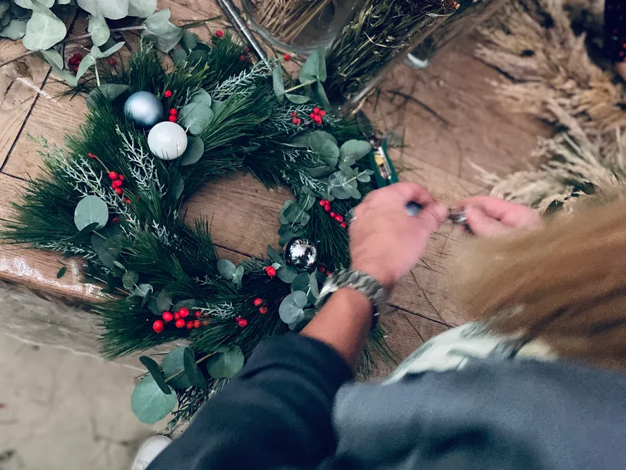 Person, die festlichen Kranz auf dem Tisch bastelt.