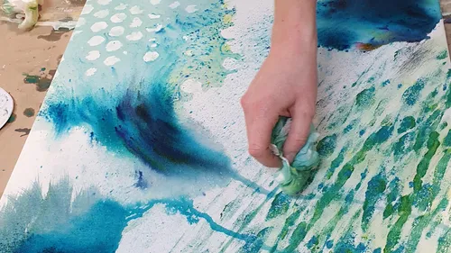 Hand verwischt blaue Farbe auf Leinwand.