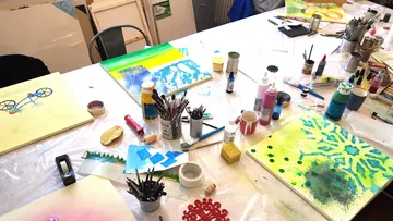 Kunstbedarf auf einem Werkstatttisch verteilt.