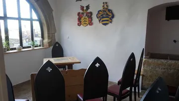 Gothic chairs around a wooden table in a medieval room.
