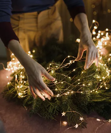 Hände arrangieren Lichter auf Weihnachtskranz.