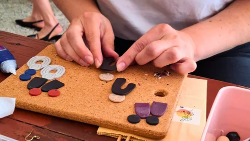 Hands crafting earrings on corkboard.