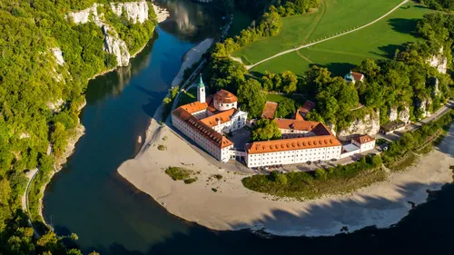 Monastery beside river in lush green valley.