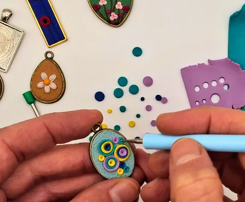 Hands crafting jewelry with colorful clay pieces.