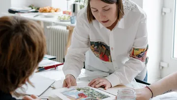 Frau zeigt Kunstwerk auf einem Tisch.